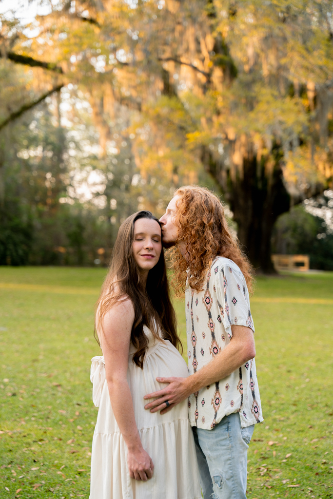 maternity photo of a woman gazing down at her baby bump with Spanish moss in the background.