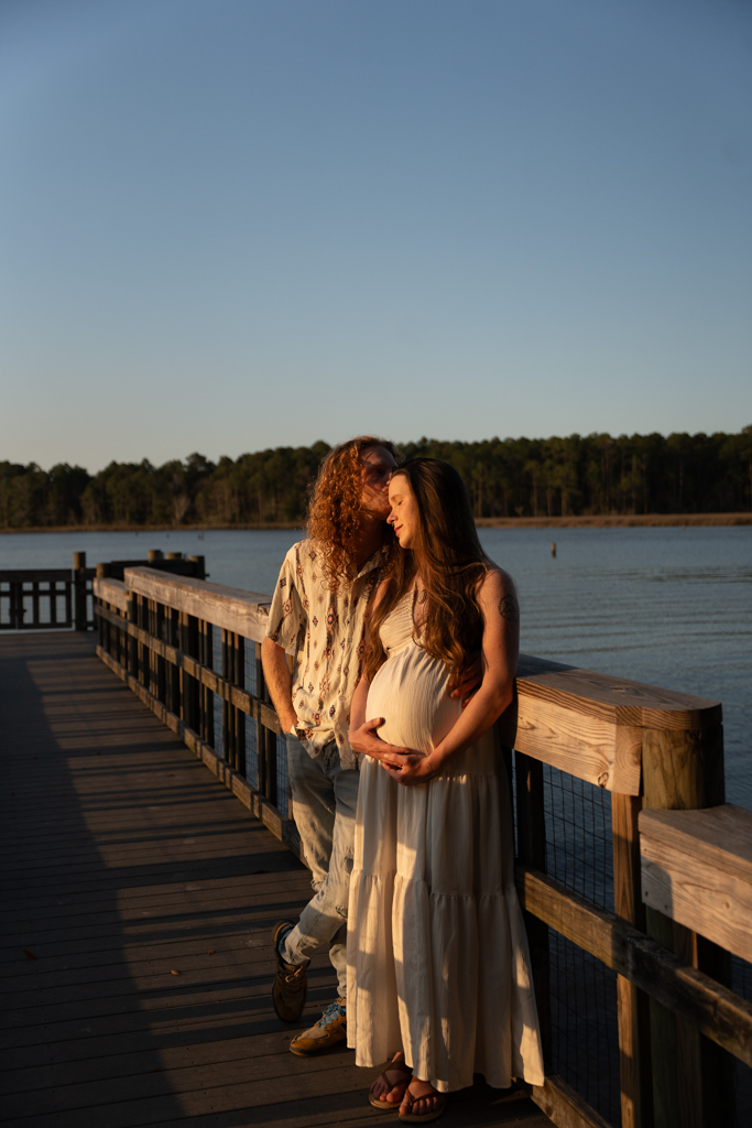 Couple standing near the reflecting pond at Eden Gardens, holding hands and smiling during a maternity session.