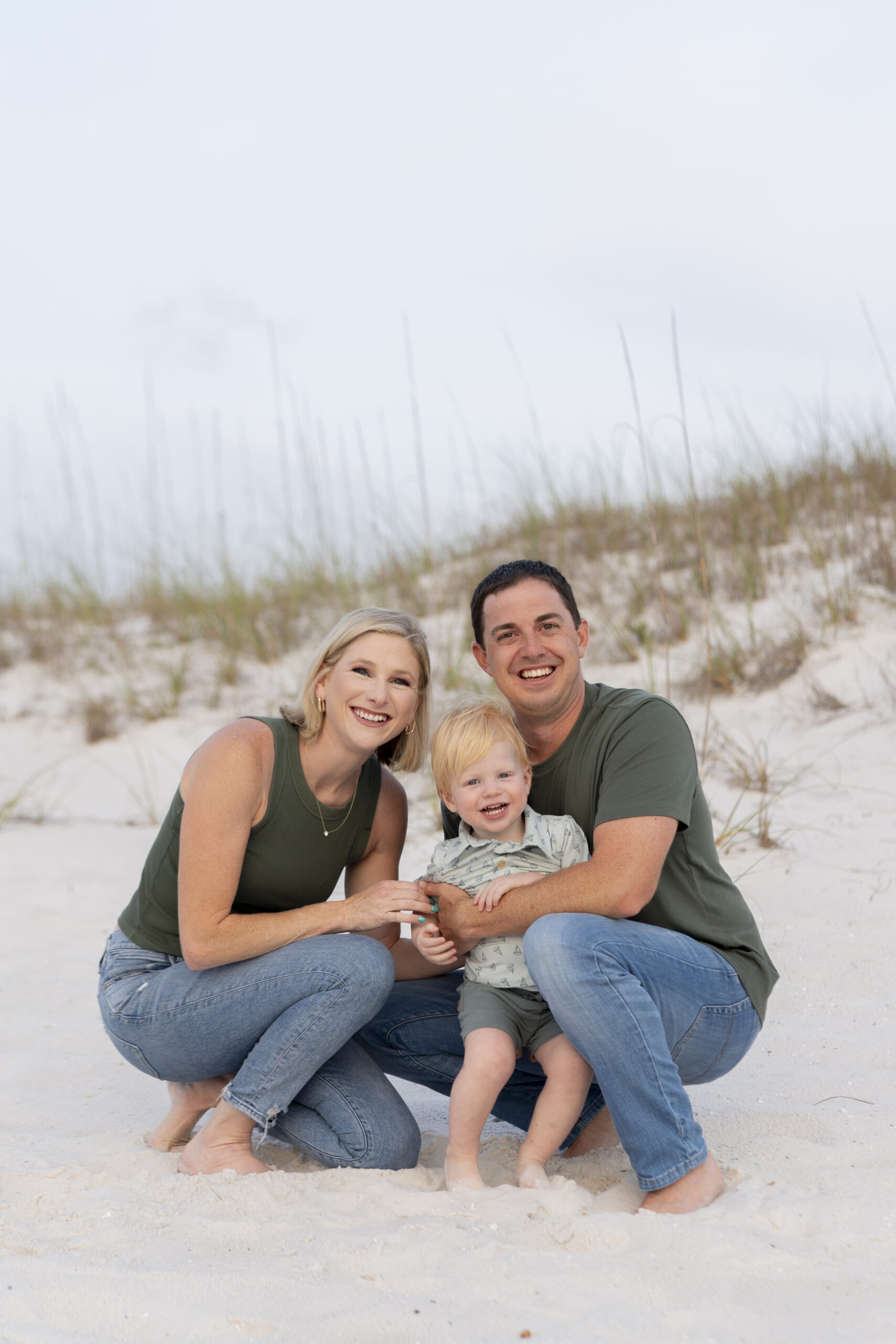 Family sitting on beach towels by the rocks at the Destin Jetties, smiling at the camera.
