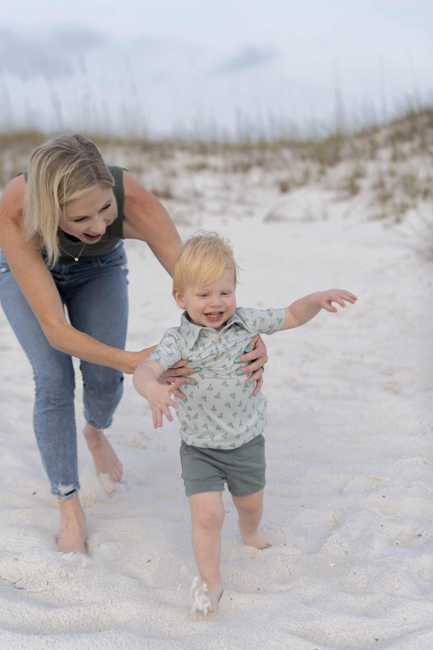 Mother holding toddler while the ocean sparkles behind them at the Destin Jetties.