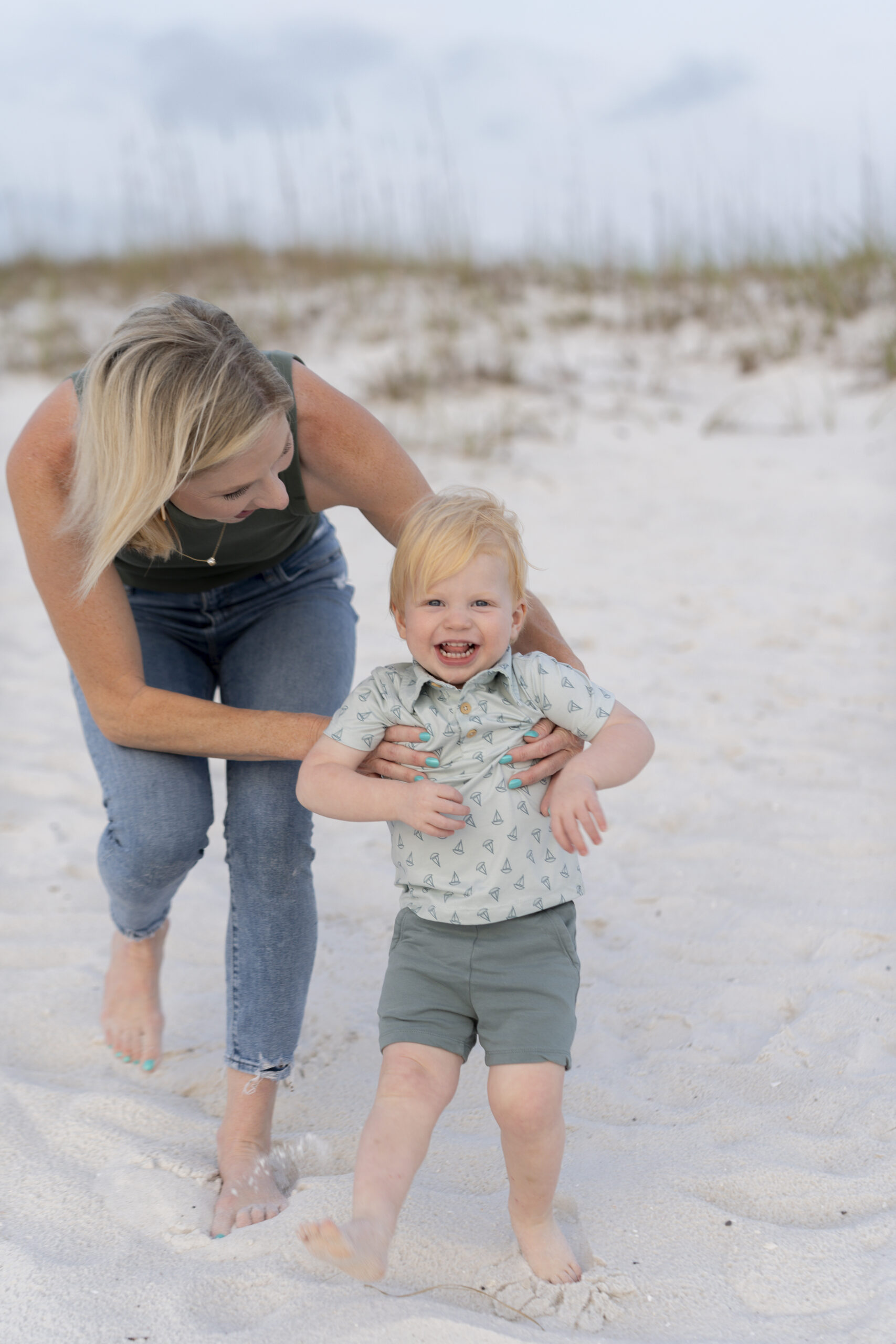 Mother holding toddler while the ocean sparkles behind them at the Destin Jetties.