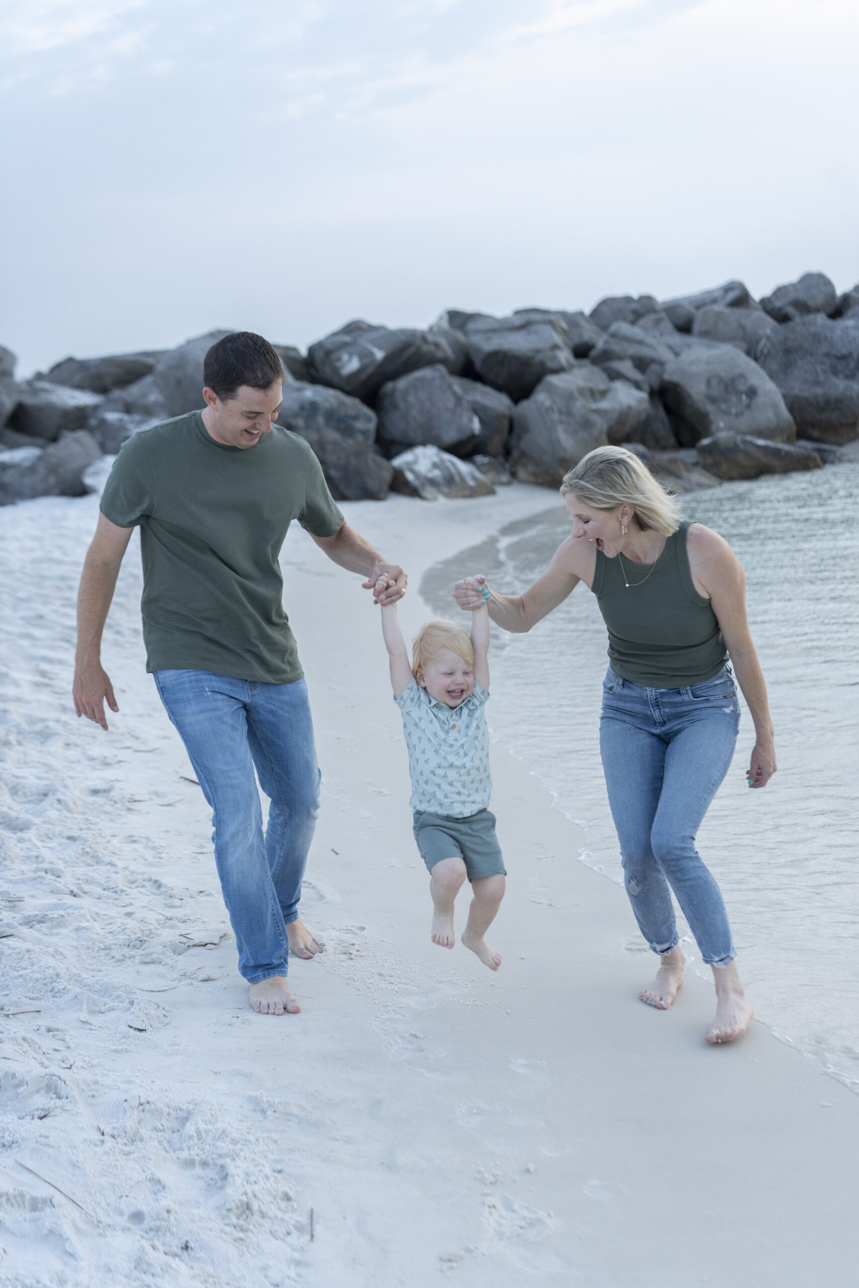 Family of three walking along the rocks at the Destin Jetties with emerald waters in the background.