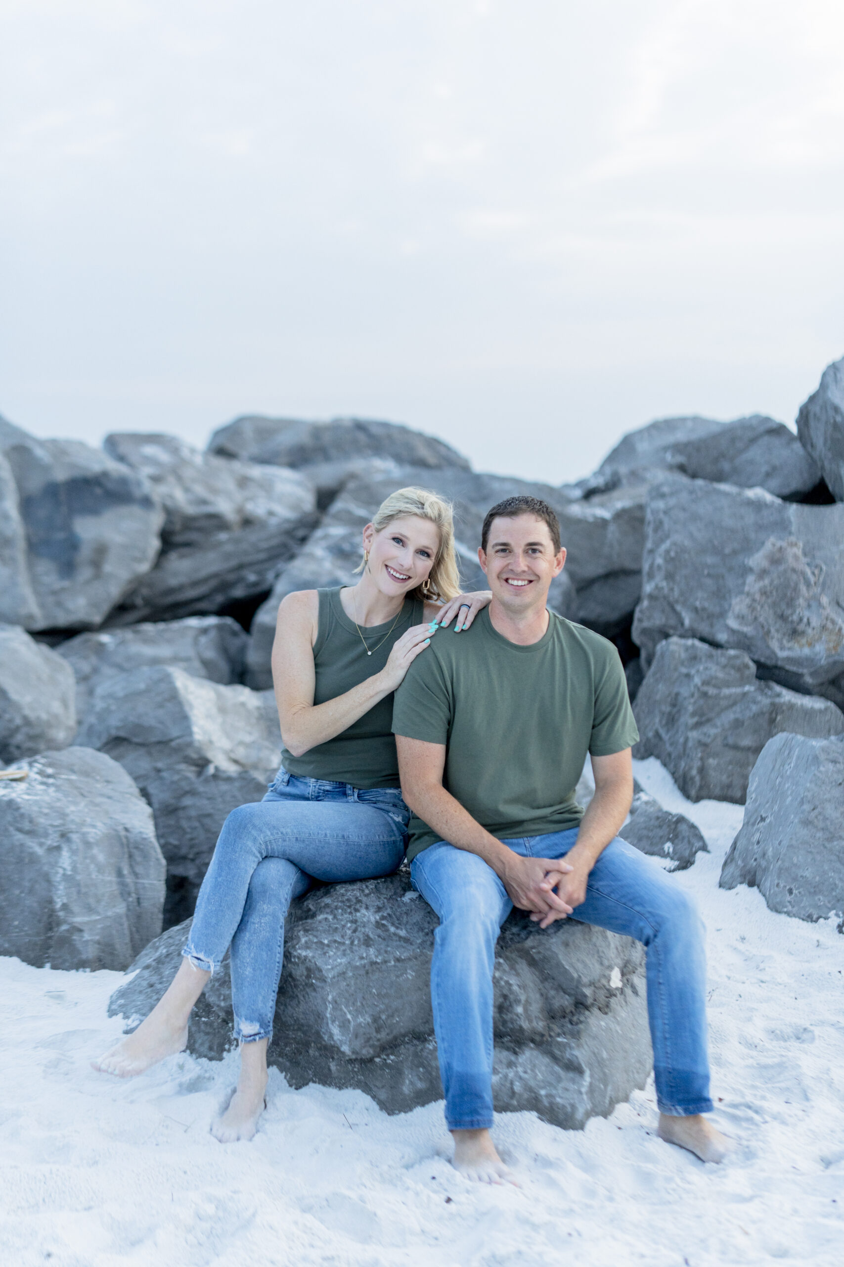 Parents looking at each other while holding their child between them, standing on the rocks at the Destin Jetties.