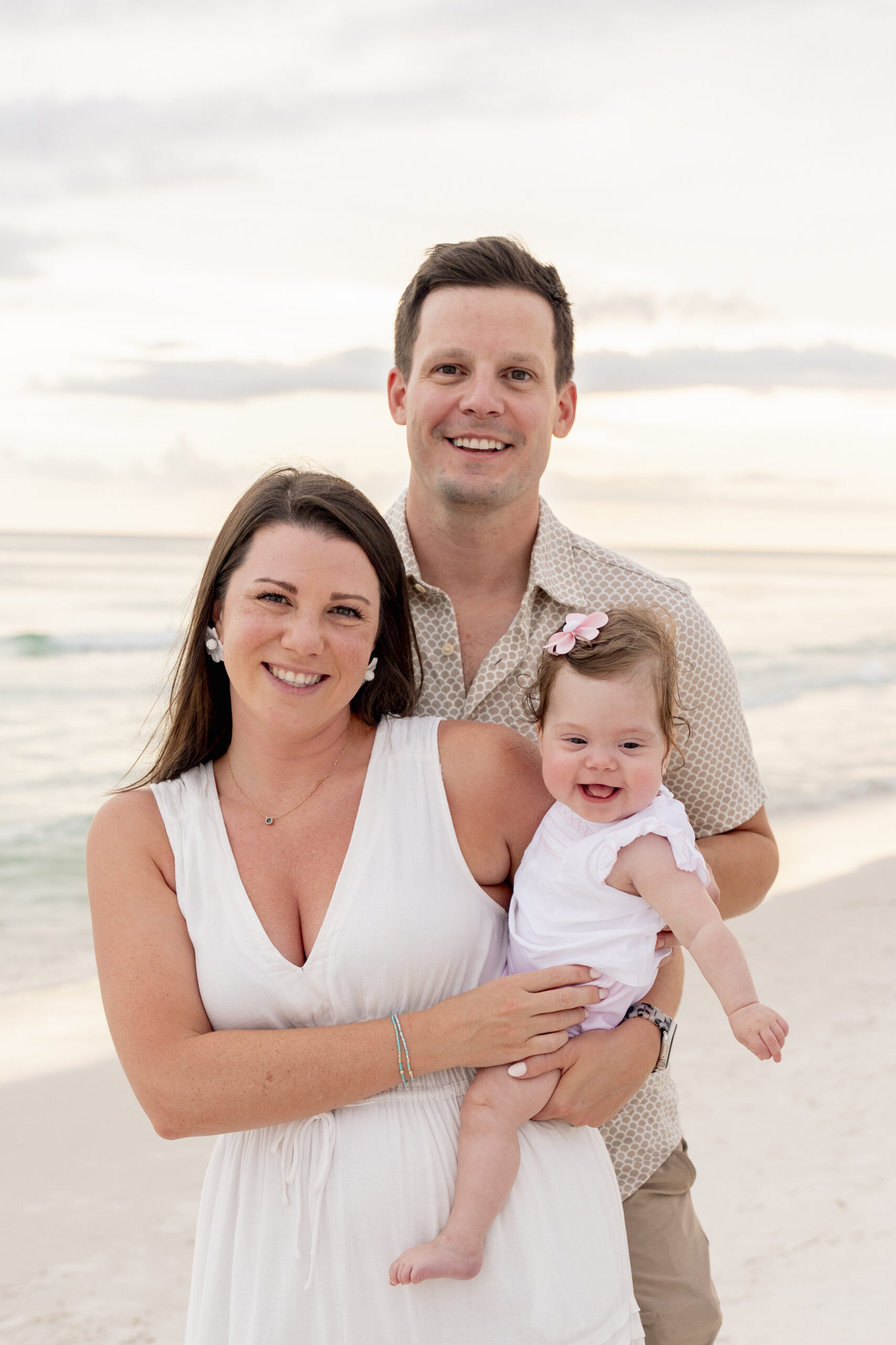 Young family of three standing barefoot at the water's edge during sunset in Inlet Beach.