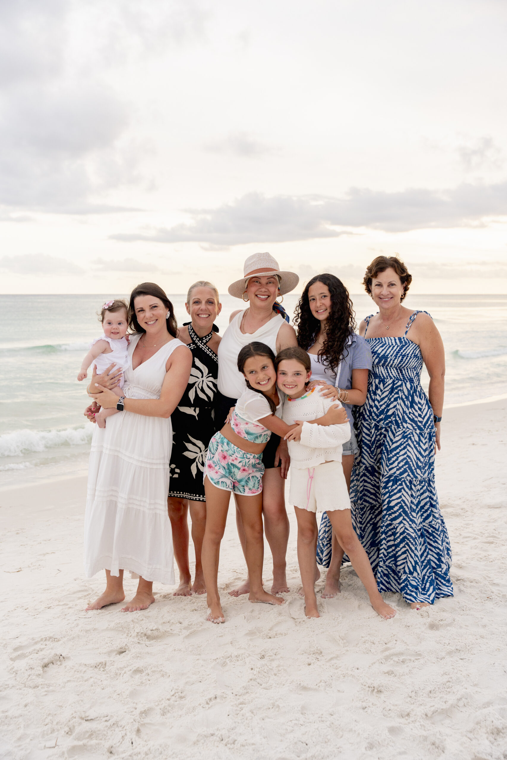 Family standing barefoot in the shallow water holding hands with the sun low on the horizon at Inlet Beach.