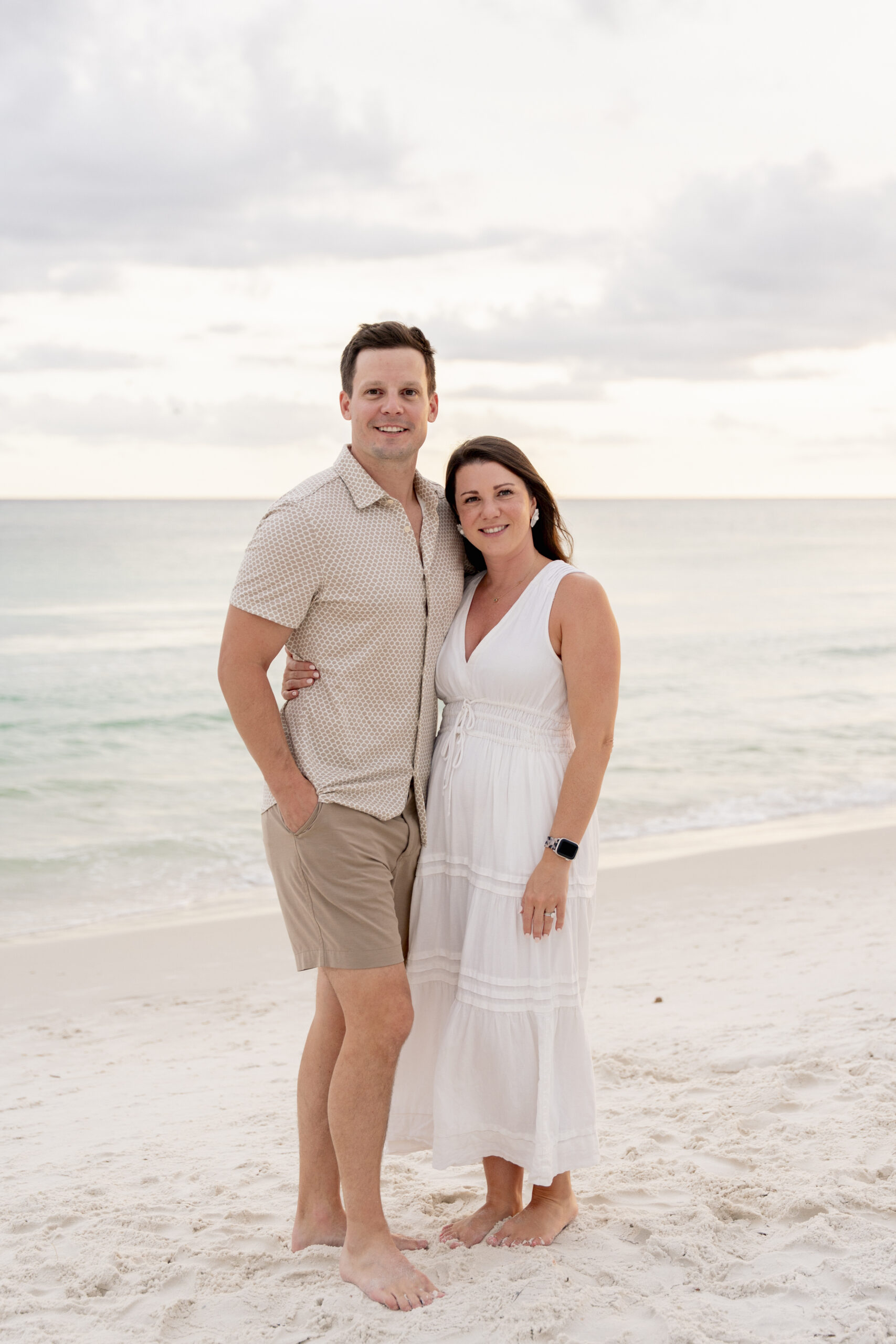Couple walking hand-in-hand along the shoreline at Inlet Beach with soft waves and a pastel sunset sky.